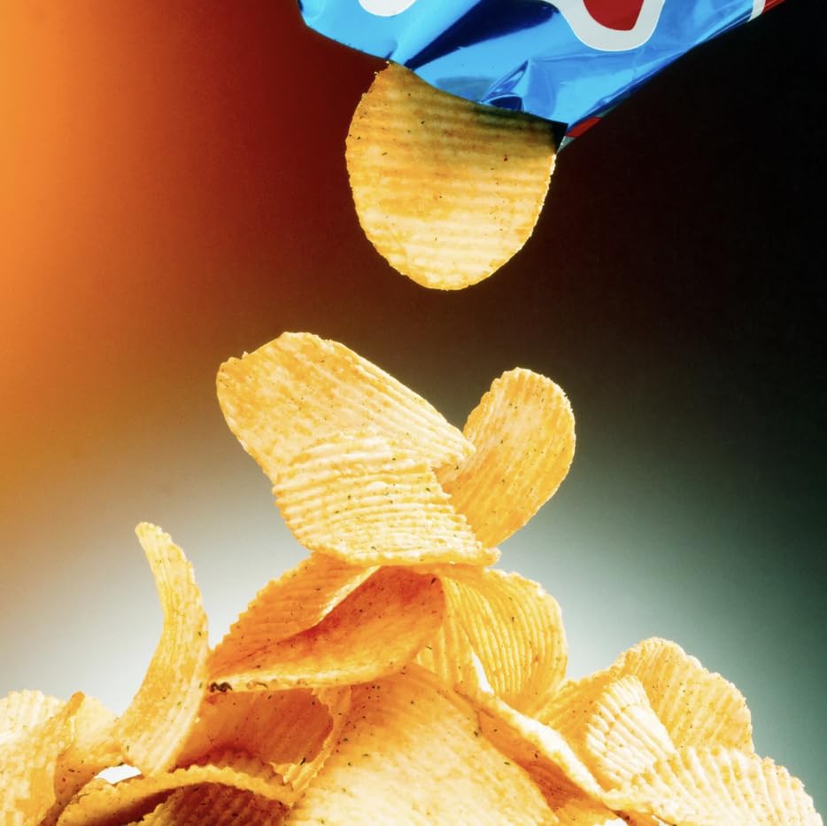 Golden potato chips falling mid-air with a snack bag in the background.