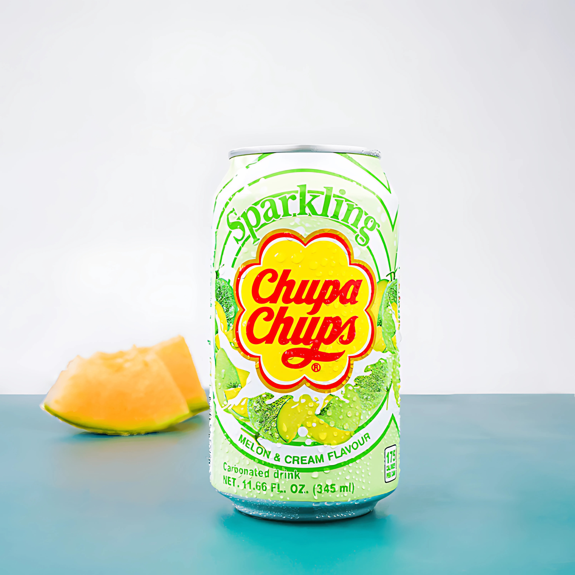 A can of Chupa Chups Sparkling Melon Cream soda is on a blue surface with a melon slice in the background.