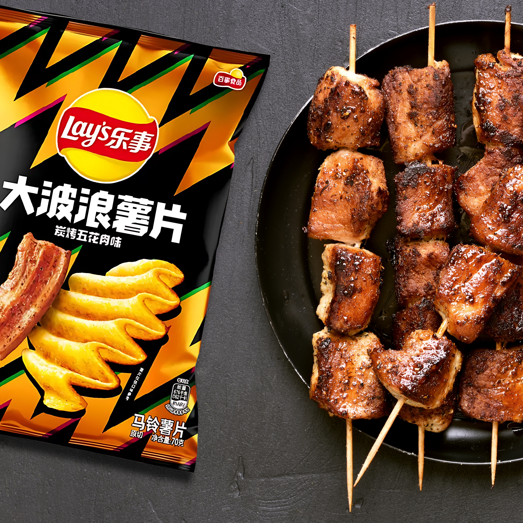 A bag of Lay's chips with bold zigzag patterns sits beside a plate of sizzling, skewered grilled pork.