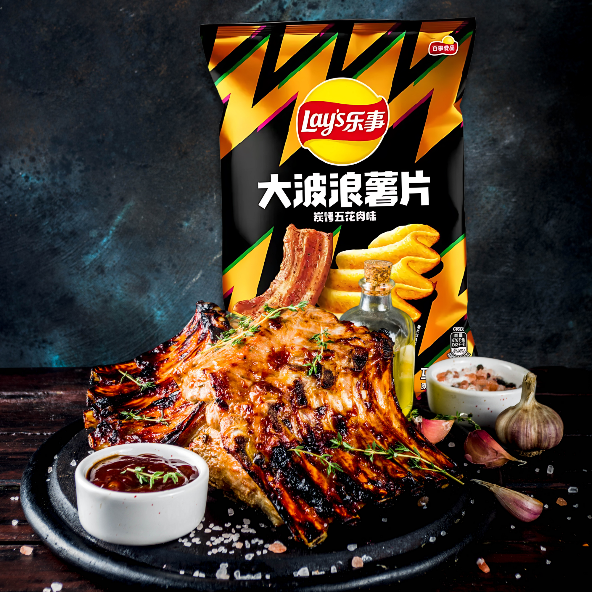 Grilled pork ribs with herbs on a black plate, surrounded by salt and sauce, are in front of a Lay's potato chips bag.