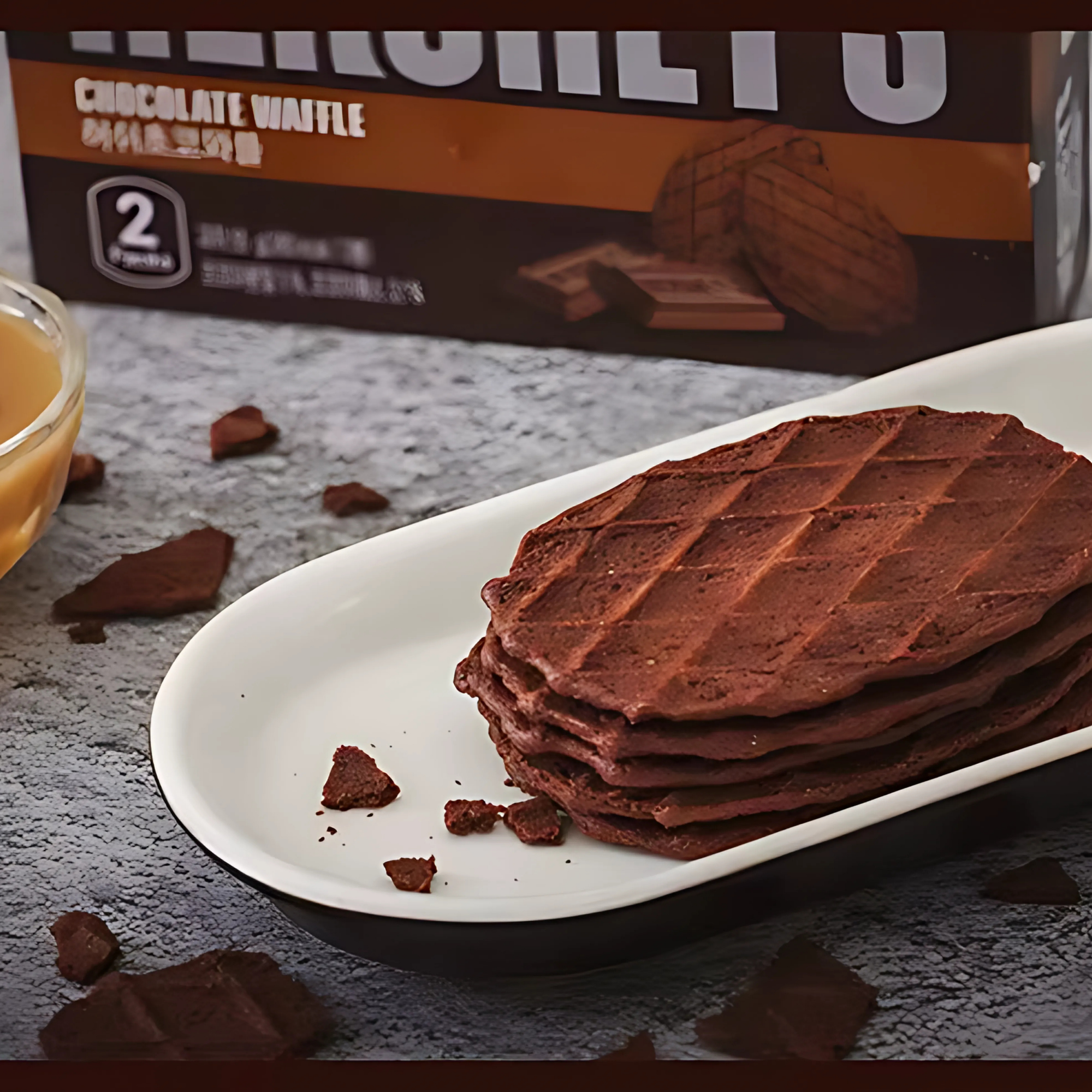 Stack of chocolate waffle cookies on a white dish with caramel sauce, Hershey’s Chocolate Waffle box in background