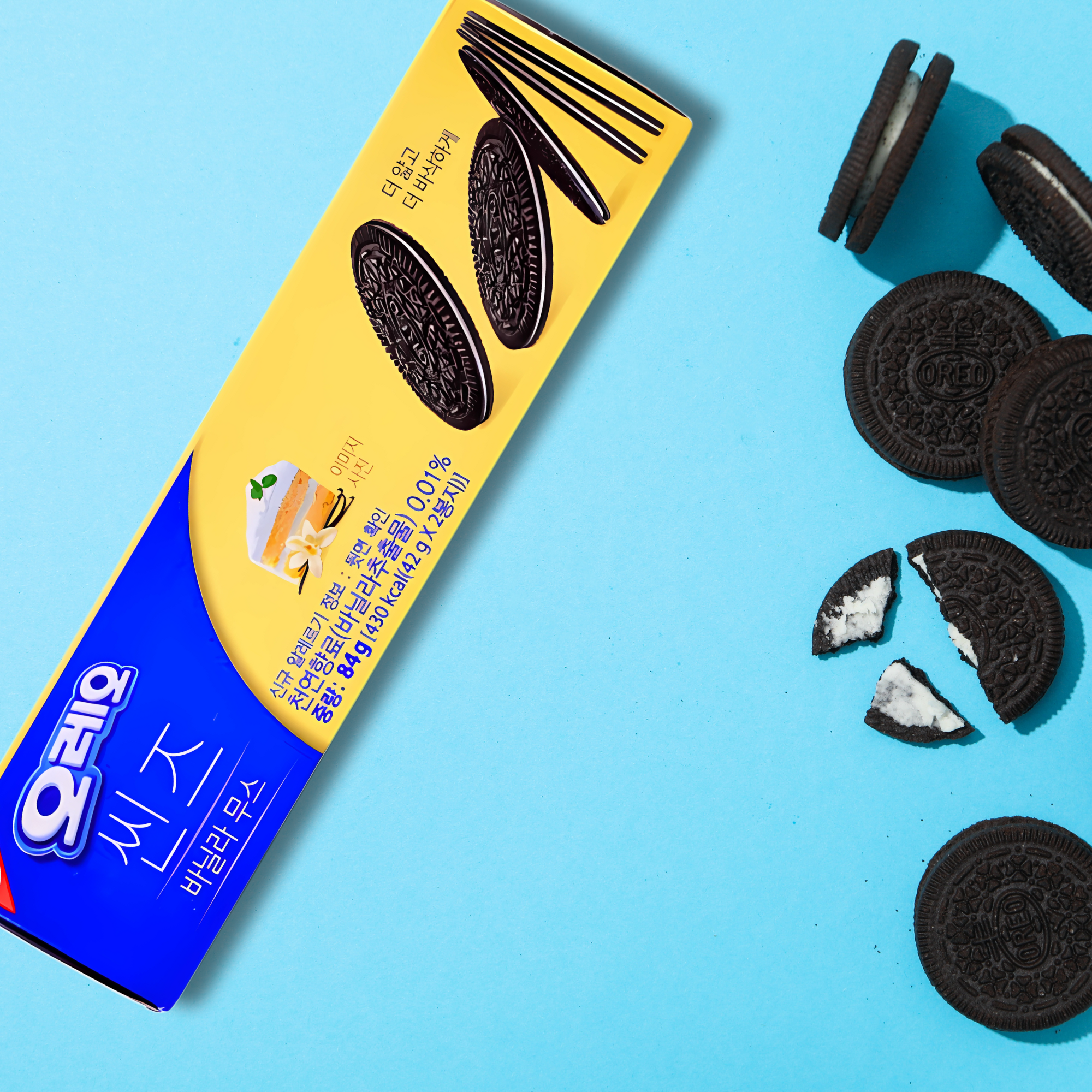 Korean Oreo Vanilla Creme sandwich cookies laid out on a pastel blue surface with Oreo cookies scattered around the box. 

