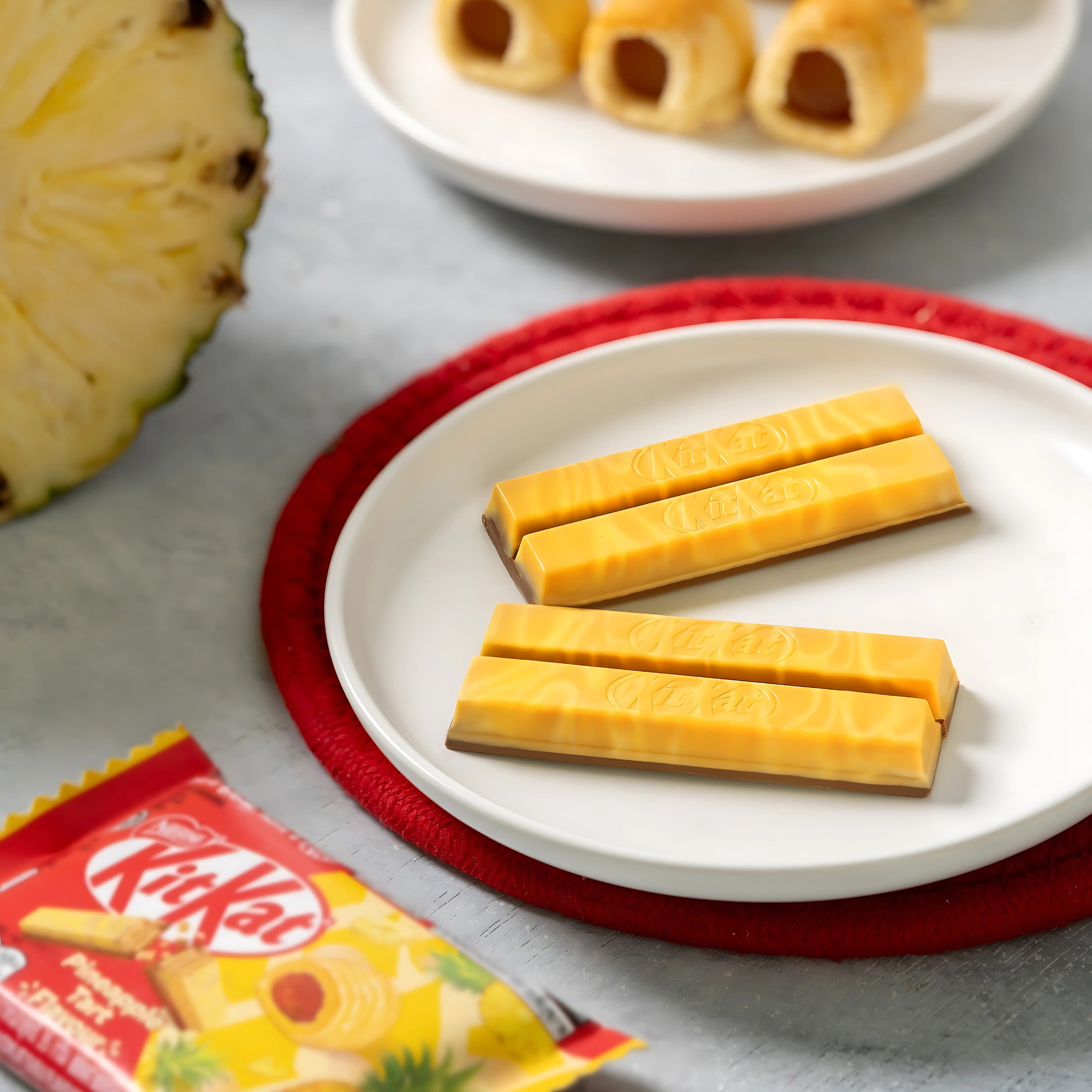 Pineapple Tart KitKat sticks on a white plate with pineapples and tart cookies in the background