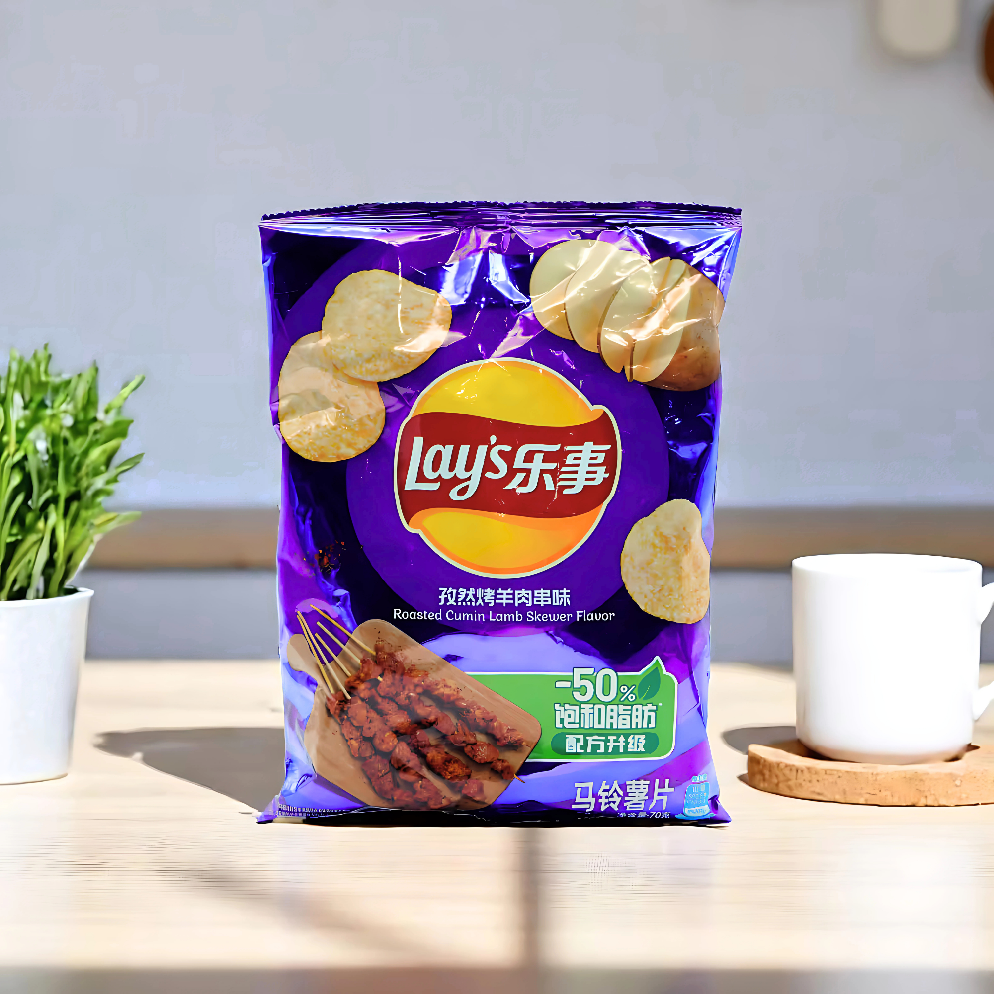 Bag of Lay's chips in Roasted Cumin Lamb Skewer flavor on a light wooden table, flanked by a white mug and a small plant. 