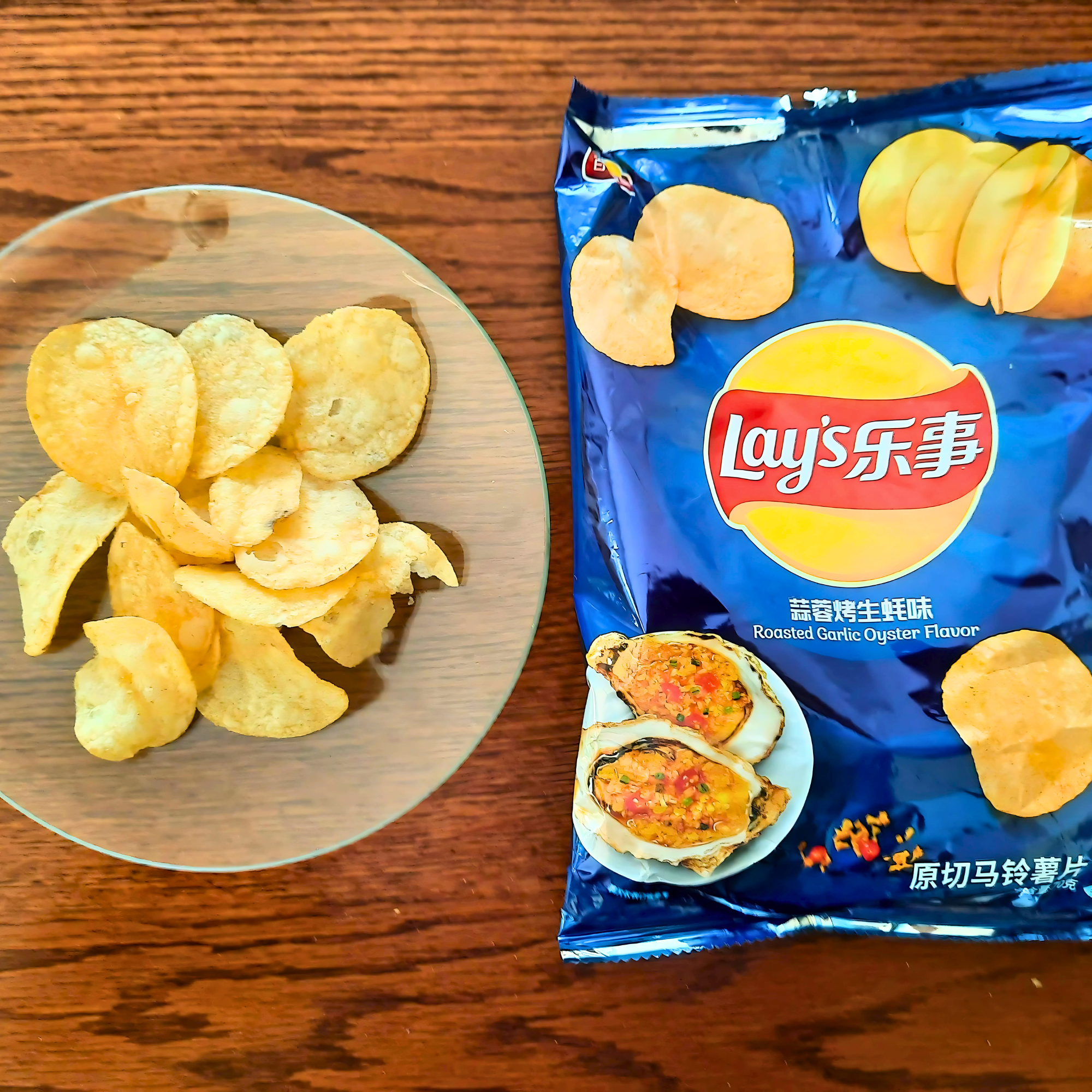 Opened bag of Lay’s Roasted Garlic Oyster flavor chips with contents poured out on a clear glass plate on a wooden table.