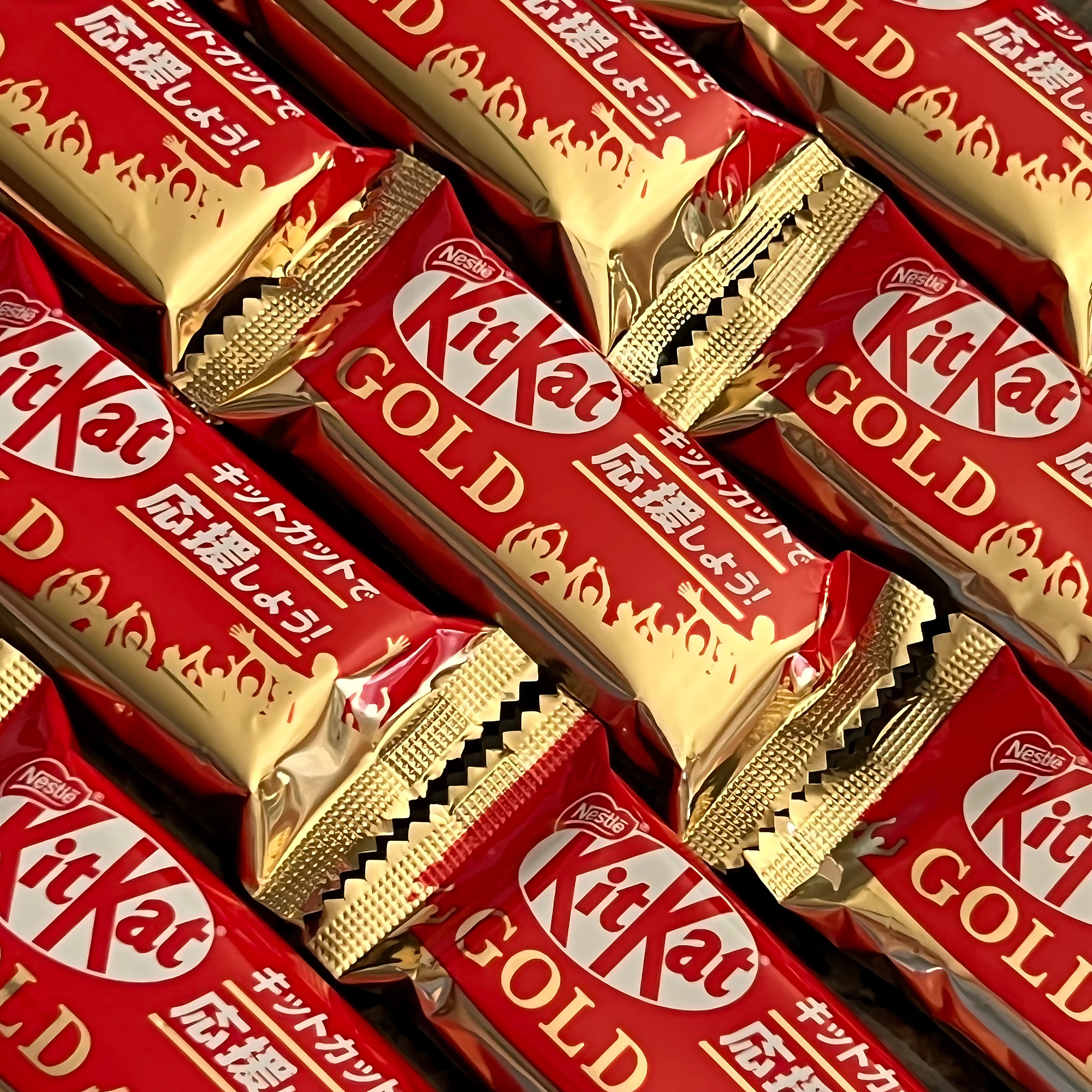 Multiple individually wrapped KitKat Gold bars in red and gold foil packaging stacked for display.