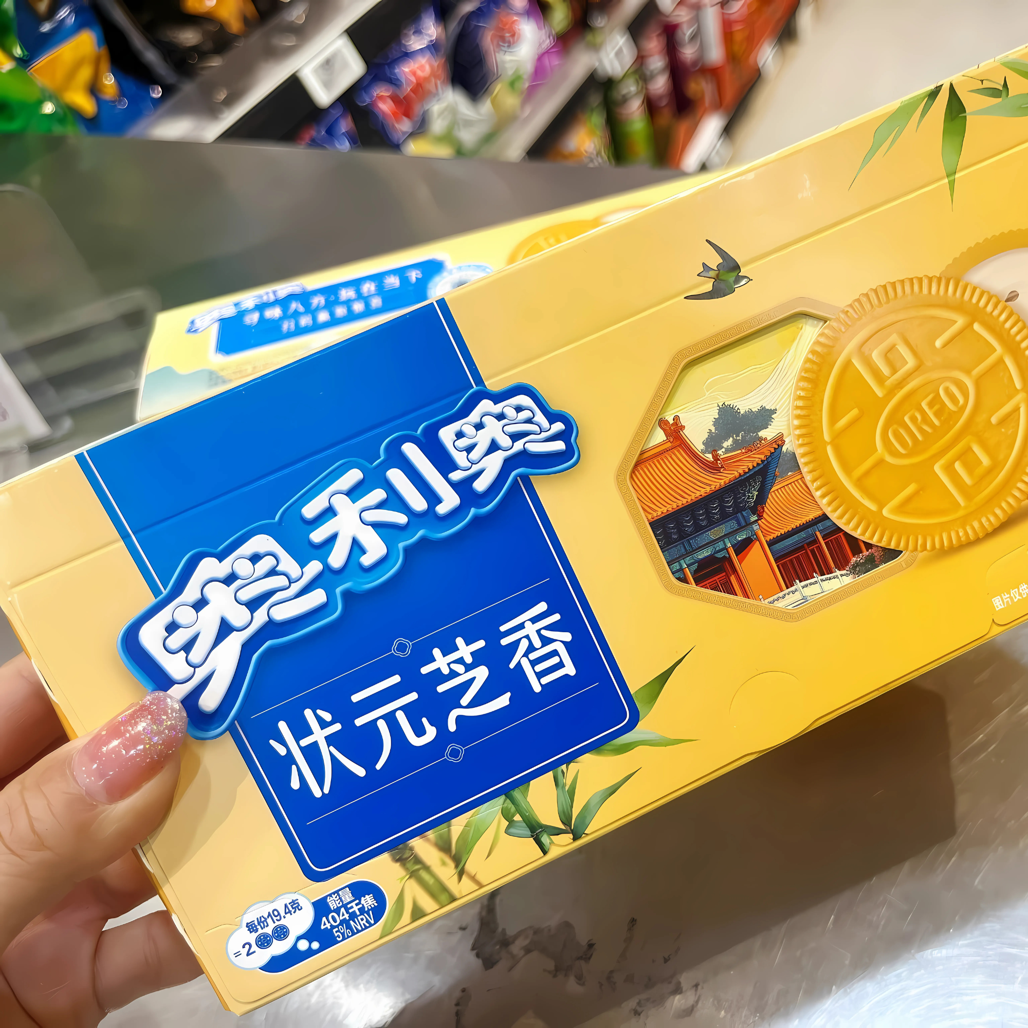 Close-up of a yellow box of Sesame Puff Pastry Milk Oreo, featuring blue Chinese text and an image of a traditional building with bamboo accents. A hand with pink nails holds the box.