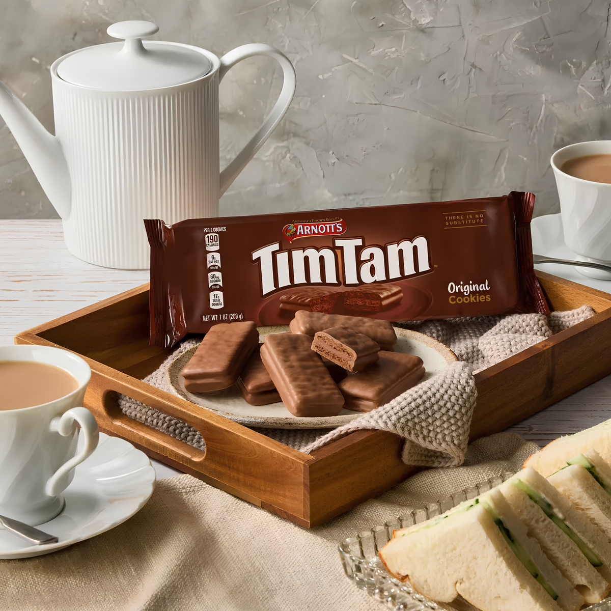 Tim Tam Original pack and chocolate biscuits on a tray with tea cups and a teapot