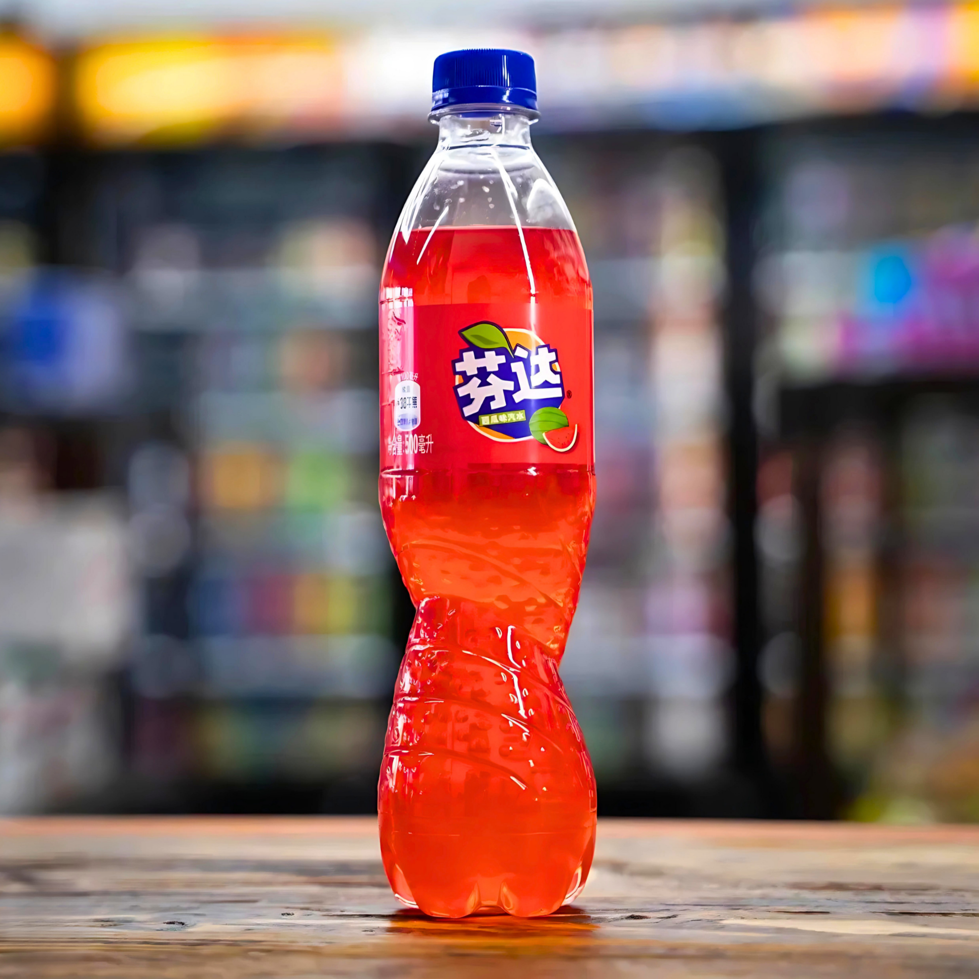 Close-up of Watermelon Fanta bottle on a wooden surface with a blurred convenience store background.