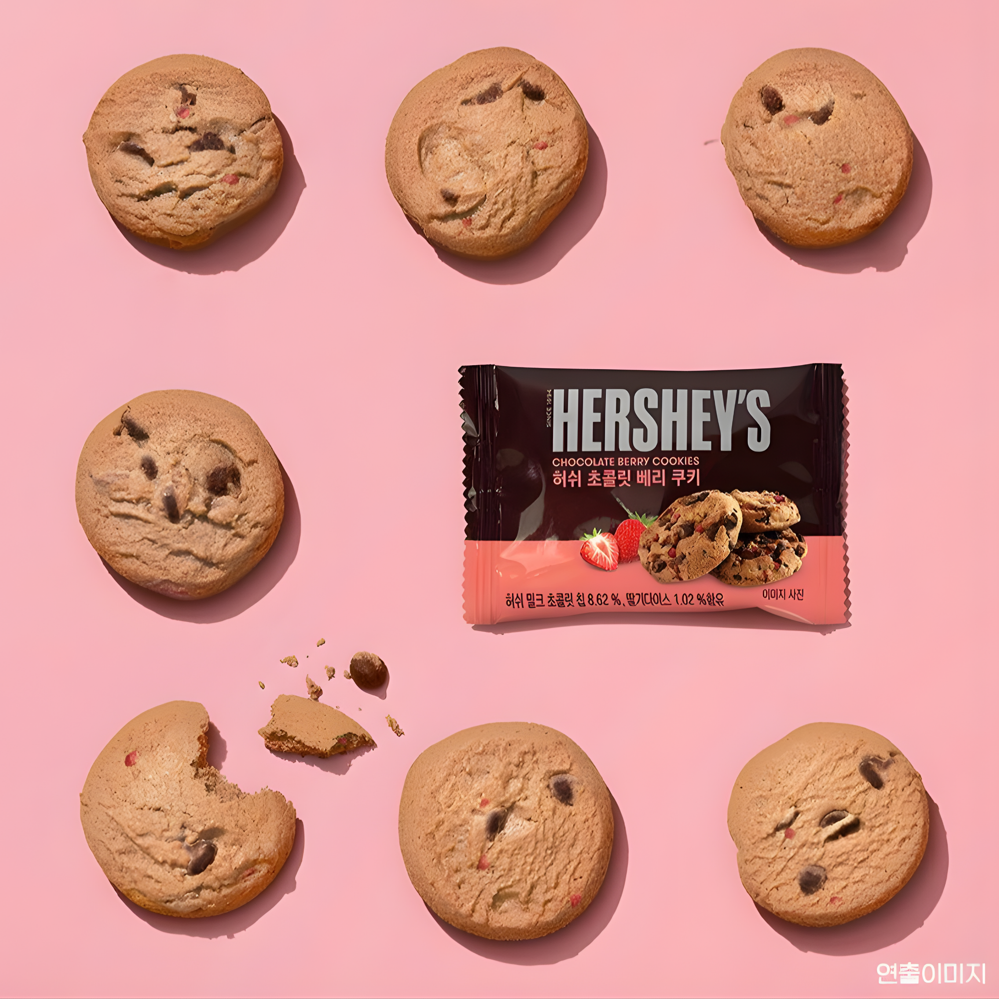 Seven chocolate chip cookies arranged on a pink background surround an Asian Hershey's chocolate berry cookies package.