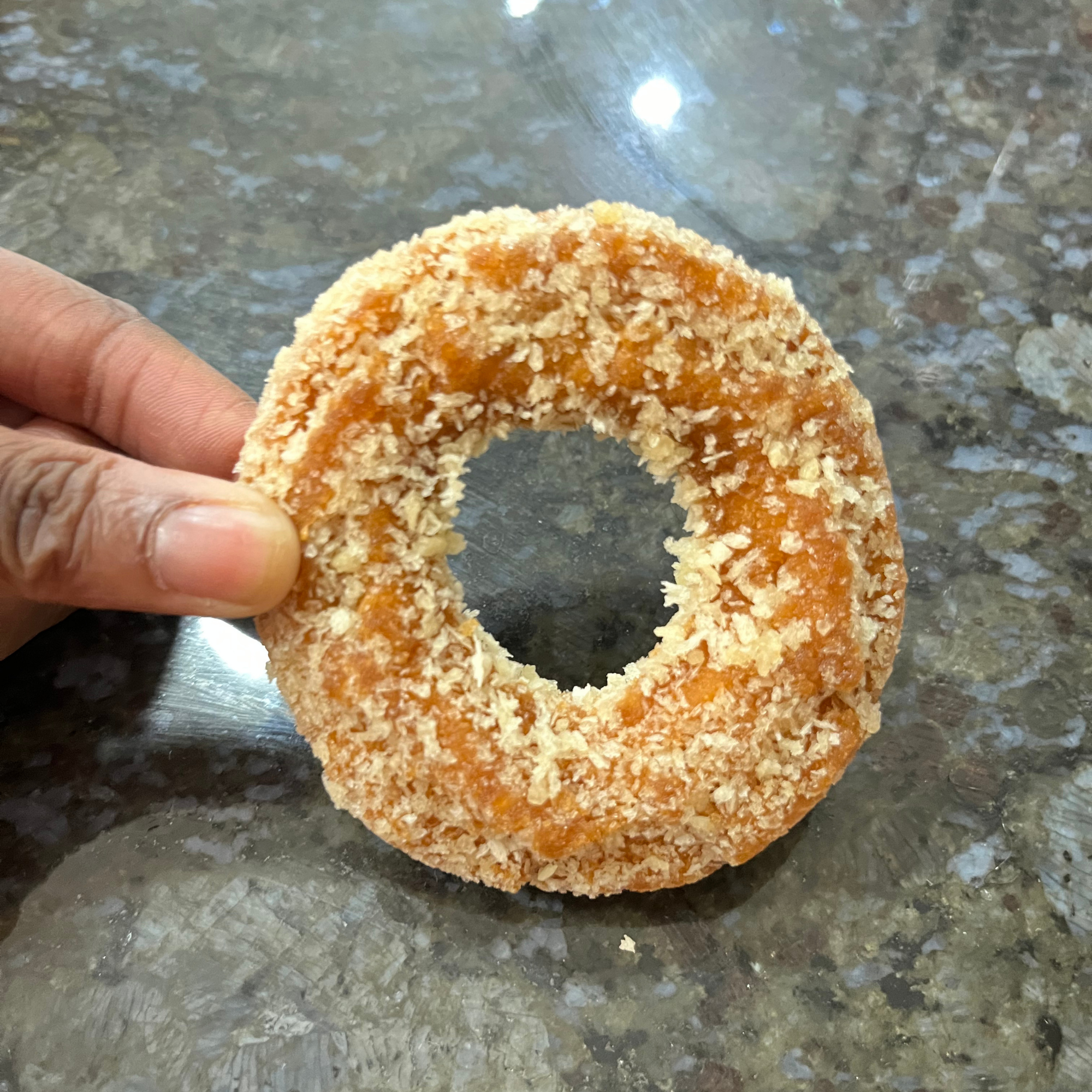 A hand holds a round, golden brown Korean Yackwa Donut against a granite surface