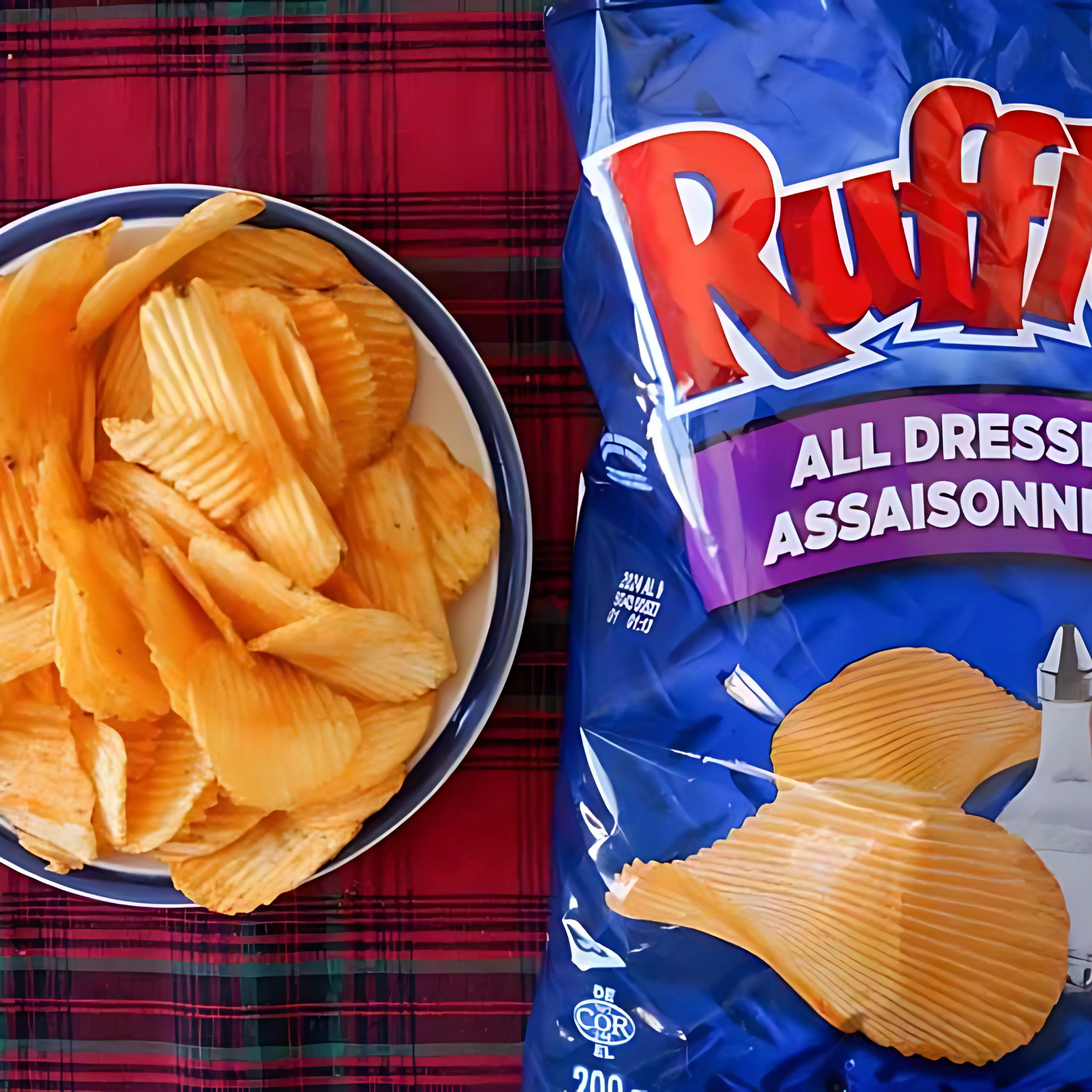 Opened Ruffles All Dressed chips bag next to a full bowl of crinkle-cut chips on plaid background.